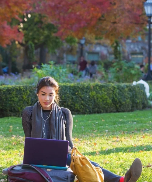 Quiet moment: student sitting on the grass with her laptop, illuminated by the sun.